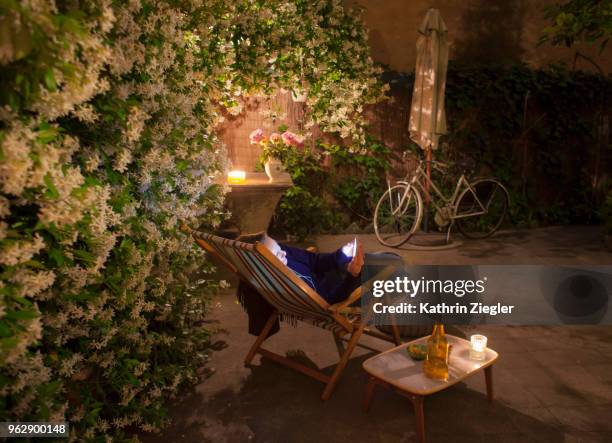 woman relaxing on deck chair in backyard, holding mobile phone - kathrin ziegler stockfoto's en -beelden