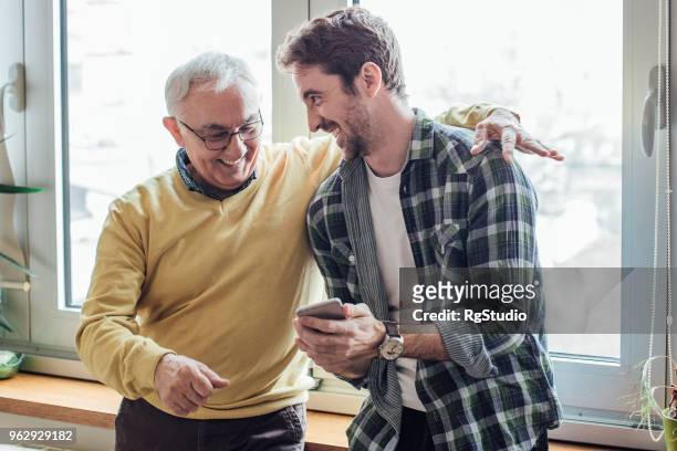 padre e figlio che ridono e usano il telefono - figlio maschio foto e immagini stock