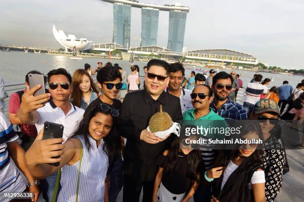 Kim Jong Un impersonator, Howard X holds the durian as he poses for a photo with tourists at Merlion Park on May 27, 2018 in Singapore. The proposed...