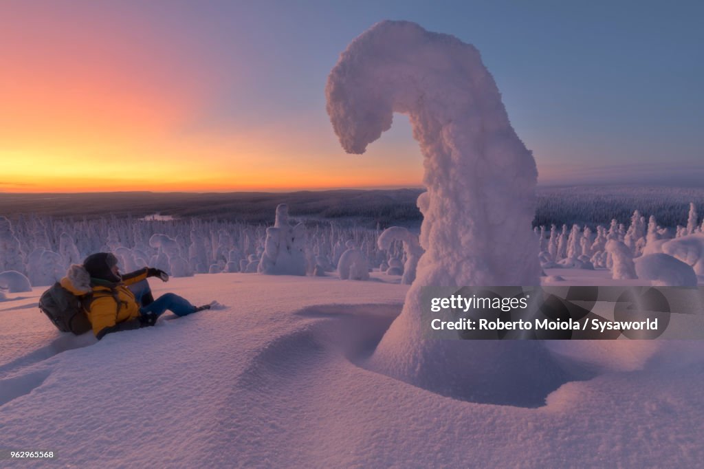 Hiker resting on the snow in the frozen forest at dusk, Riisitunturi National Park, Posio, Lapland, Finland