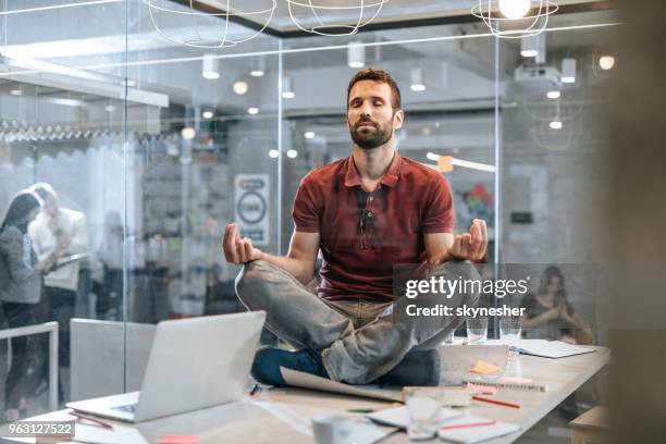 young relaxed male entrepreneur exercising yoga on the table in the office. - businessman meditating stock pictures, royalty-free photos & images