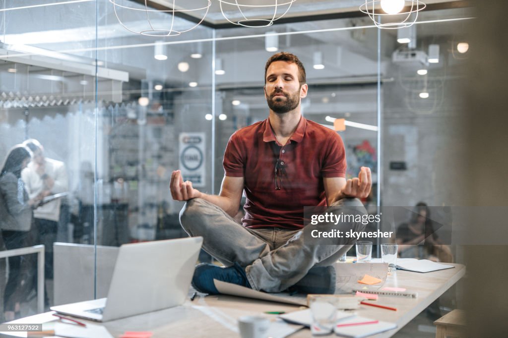 Jovem relaxado masculino empresário exercício Yoga em cima da mesa no escritório.