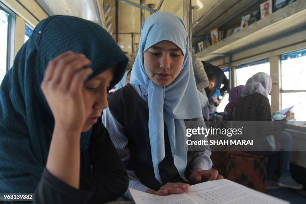 In this photograph taken on April 4 Afghan girls read books in a mobile library bus in Kabul. - The door of the blue bus slides open and dozens of...