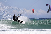Man in a black wetsuit kitesurfing on the ocean waves