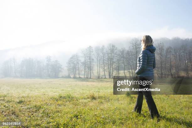 woman walks through hilly meadow in mist - woman jacket stock pictures, royalty-free photos & images