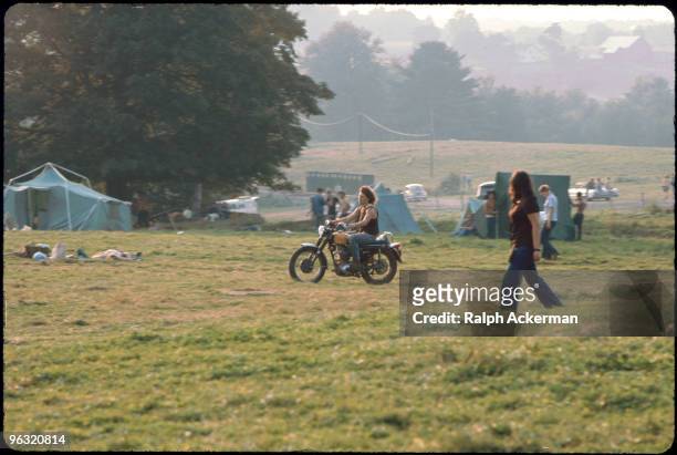 Michael Lang rides his motorcycle through the grassy camping area as people put up tents and lie on the grass at the Woodstock music festival, August...