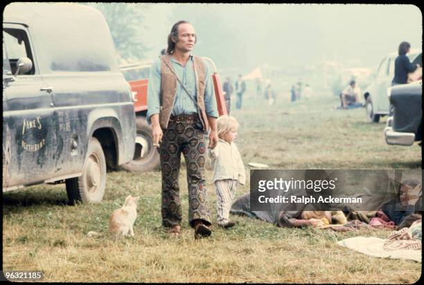 Man and a child walking past people in sleeping bags at the Woodstock music festival, August 1969.