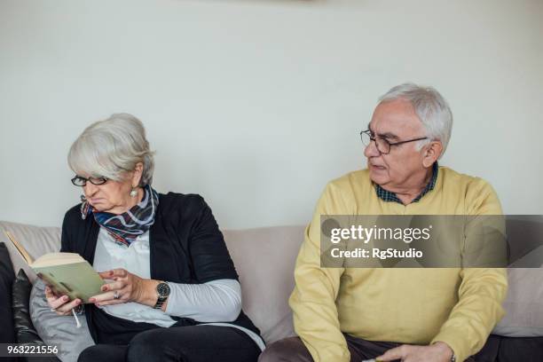 ältere mann seine frau wütend anzuschreien, während sie ein buch liest - grumpy old man stock-fotos und bilder