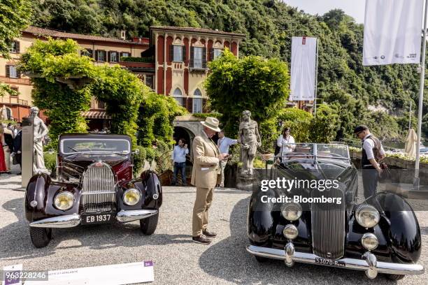 Visitor stands between a 1937 Bugatti Automobiles SAS 57 Atalante, left, and a 1936 Lancia Automobiles SpA Astura Serie III at the 2018 Concorso...