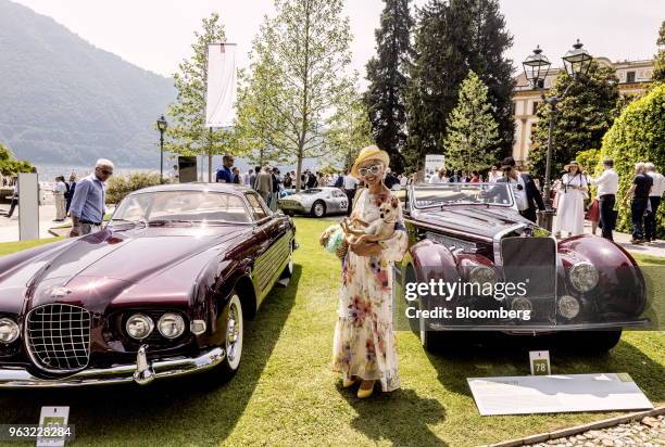 Visitor poses for a photograph between a 1939 General Motors Co. Cadillac Series 62, left, and a 1939 Delage D8-120 at the 2018 Concorso D'Eleganza...