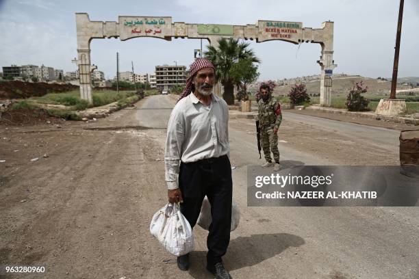 Syrian man walks as armed men stand guard the city's entrance in Afrin, on May 5, 2018.