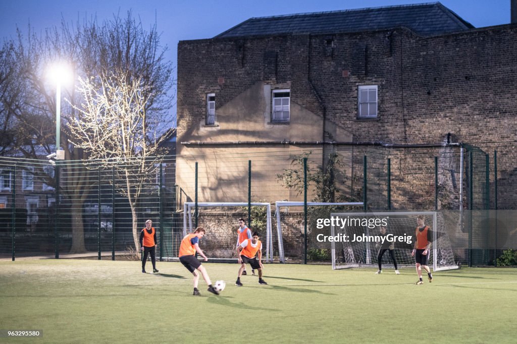 Outdoor urban floodlit pitch with group of men playing football