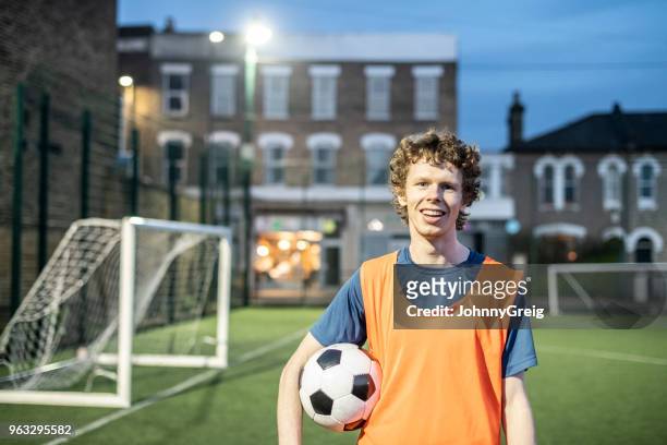 junger mann in seinen 20ern tragen orange fußball lätzchen und holding ball unter arm - flutlicht stock-fotos und bilder