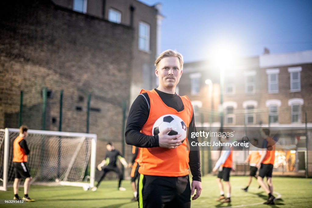 Porträt von zuversichtlich Fußballspieler in seinen 30ern halten Fußball auf Platz in der Nacht