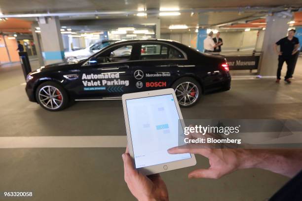 An attendee uses an app on an Apple Inc. IPad tablet computer as a driverless Daimler AG Mercedes-Benz AMG E63 S automobile maneuvers to a parking...