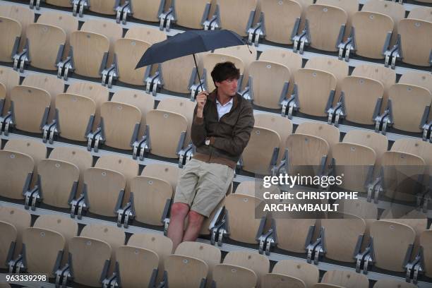 Spectator shelters from the rain under an umbrella as he waits for the start of the women's singles first round match between Russia's Maria...