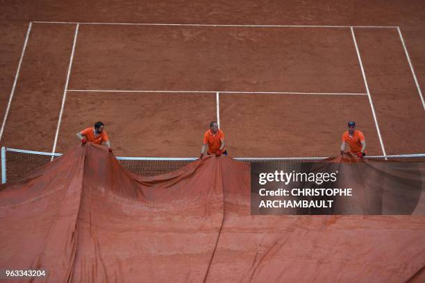 Groundstaff members pull covers across the court surface as rain falls prior to the start of the women's singles first round match between Russia's...