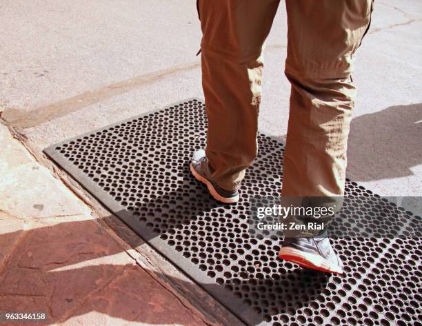 adult man wearing convertible travel pants walking on metal grid drain cover - metal grate fotografías e imágenes de stock