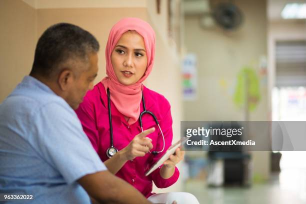 weiblichen muslimischen arzt rücksprache mit einem patienten - indonesian ethnicity stock-fotos und bilder