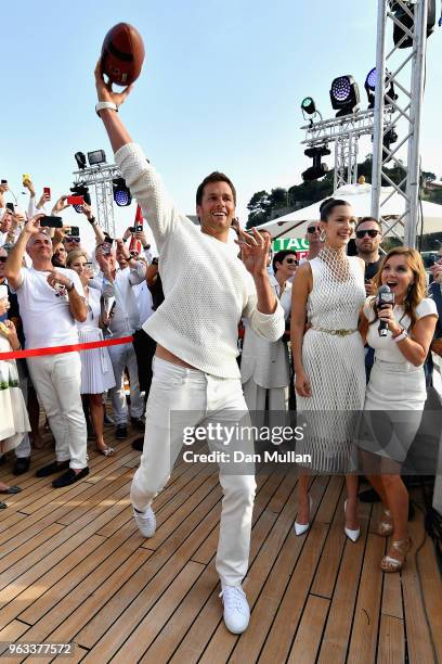 Star Tom Brady throws a ball to Daniel Ricciardo of Australia and Red Bull Racing on the TAG Heuer boat after qualifying for the Monaco Formula One...