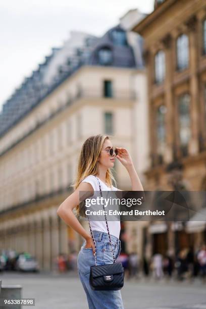 Rosa Crespo, fashion blogger, wears Quay sunglasses, a white t-shirt, blue denim jeans, a Chanel black leather bag, on May 27, 2018 in Paris, France.