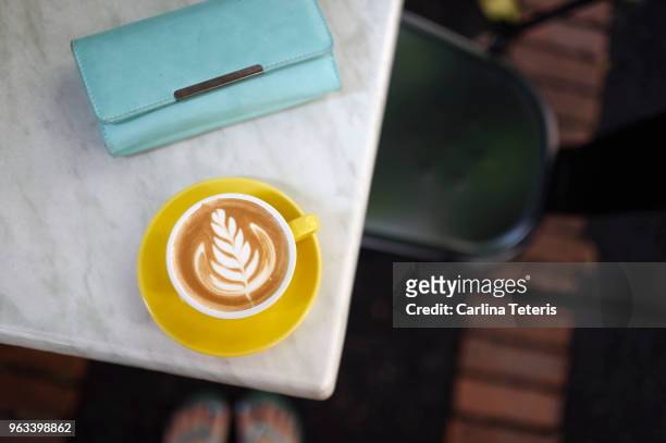 latte art in a yellow cup on a cafe table with a ladies wallet - blue purse stock pictures, royalty-free photos & images
