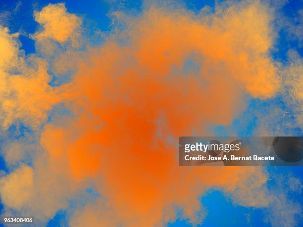 full frame of forms and textures of an explosion of powder and smoke of color yellow and orange on a light blue background. - yellow light effect stock pictures, royalty-free photos & images