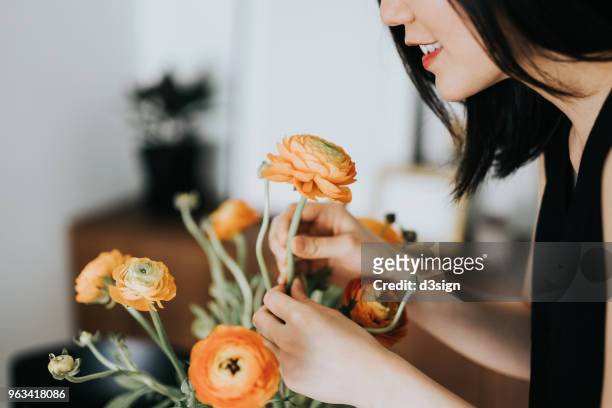 woman smelling flowers while arranging it at home - arrangiare foto e immagini stock