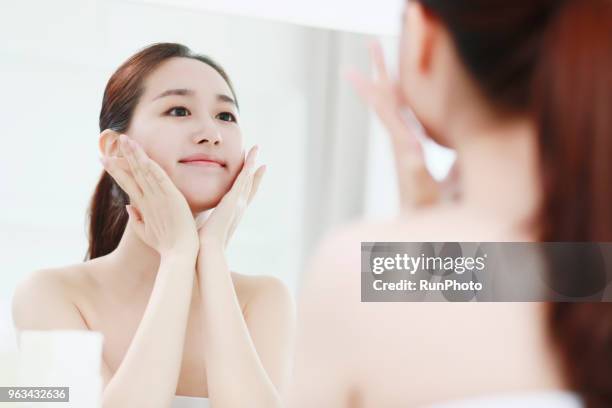 young woman looking in mirror, touching face - beautification fotografías e imágenes de stock