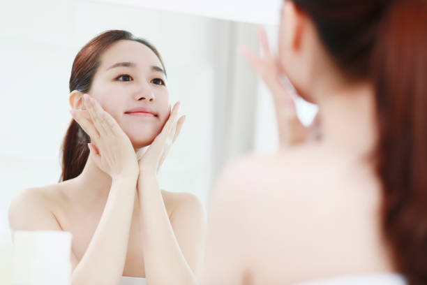 Young woman looking in mirror, touching face