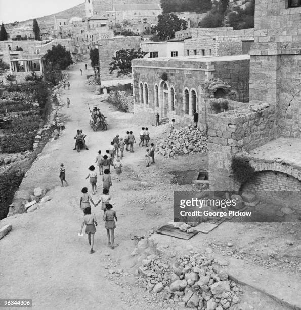 Teenage students on their way to school at Ein Kerem in southwest Jerusalem, Israel, circa 1955. The buildings on the right show damage dating from...