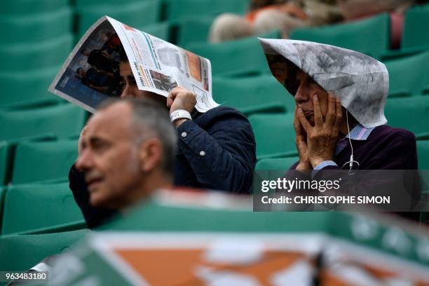 Spectators shelter under newspapers as rain falls during the men's singles first round match between Croatia's Marin Cilic and Australia's James...