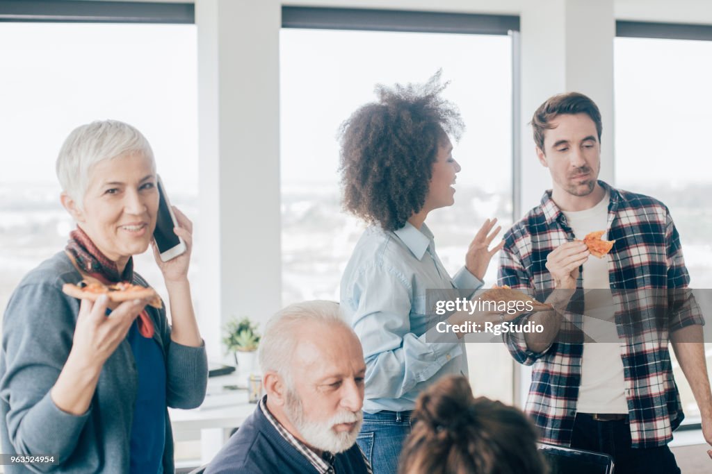 Zakenvrouw met behulp van de mobiele telefoon en pizza delen met collega 's
