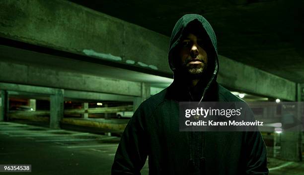 portrait of hooded man in empty parking garage - kapuze stock-fotos und bilder