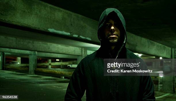 portrait of hooded man in empty parking garage - acosador fotografías e imágenes de stock