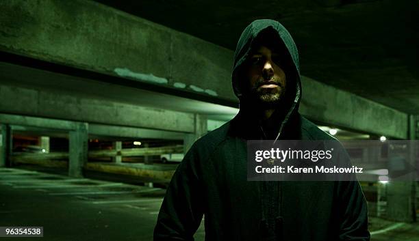 portrait of hooded man in empty parking garage - stalker foto e immagini stock