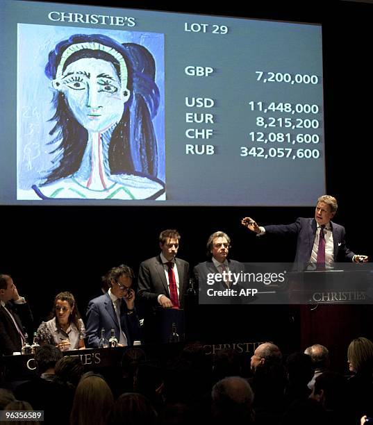 An auctioneer speaks as a painting entitled 'Tete de femme' of Spanish painter Pablo Picasso is displayed on a screen behind him during a Christies...