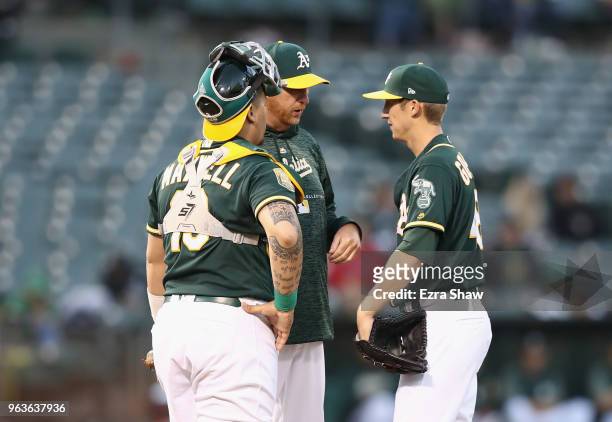 Pitching coach Scott Emerson and catcher Bruce Maxwell come out to talk to Daniel Gossett of the Oakland Athletics after he gave up three home runs...