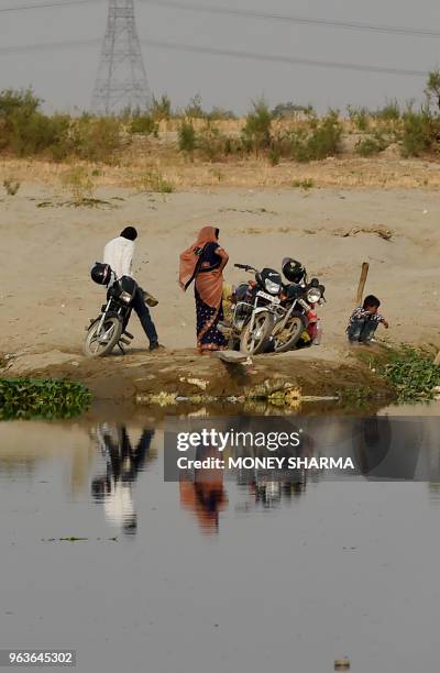 In this photograph taken on May 29 Indian commuters wait for a boat taxi to arrive on the banks of the Yamuna river in Manjhawali village, some 25kms...