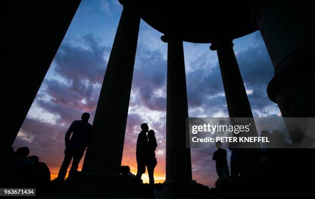 People stand between the columns of the Monopteros round temple at the Englischer Garten park in Munich, southern Germany, as sun sets on May 29,...