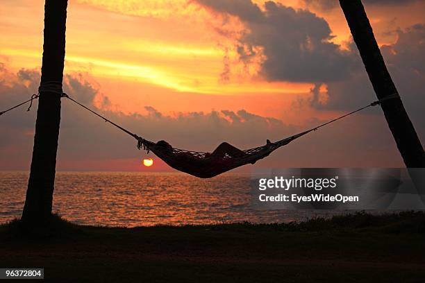 Woman relaxes in a hammock between two palm trees at sunset on the beach of Varkala. On January 12, 2010 in Varkala near Trivandrum, Kerala, India.