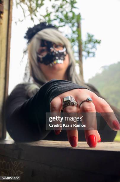 high resolution photography of caucasian young woman, featuring a mask of shiny black teeth on her eyes and nose, white and black hair wig on natural daylight background, and hand with red nails and rings in may 2018, in folkloric celebration of witches' - black hair wig stock pictures, royalty-free photos & images