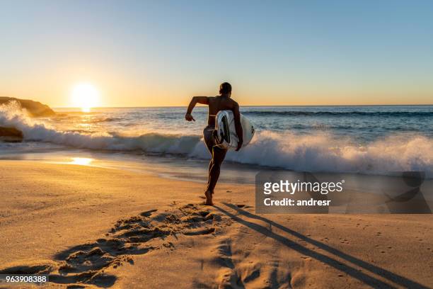 surfer lopen in het water zijn bestuur te voeren - beach sunrise stockfoto's en -beelden