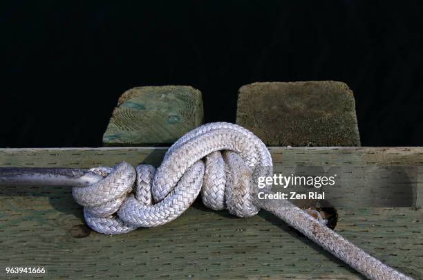 white mooring line tied securely in a knot on metal bar in a wooden mooring dock - anlegetau stock-fotos und bilder