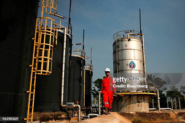 Exploration & Production Pcl production operator Kowan Boonruangjal walks past crude oil storage tanks, left, and the tank where oil is separated...