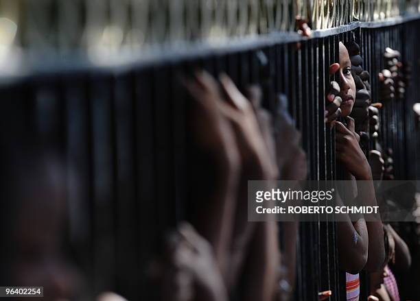 Haitian girl living in a makeshift camp at a park looks through the bars of the park at a memorial service held in front of the collapsed Ministry of...