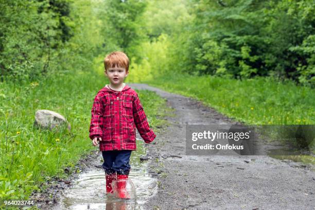 young cute kid walking jumping into water puddle - onfokus stock pictures, royalty-free photos & images