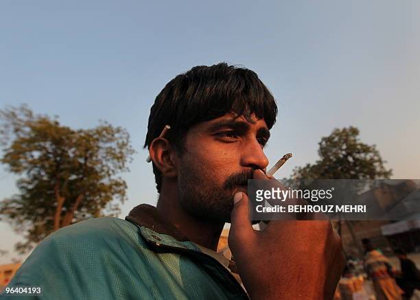Pakistani Muslim devotee sufi smokes a cannabis cigarette in a Christian grave yard next to the Data Darbar where is the Saint Syed Ali bin Osman...