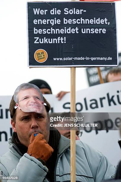 Protestor wearing a mask of German Environment Minister Norbert Roettgen holds a placard reading "The one who cuts the solar energy, cuts our future"...