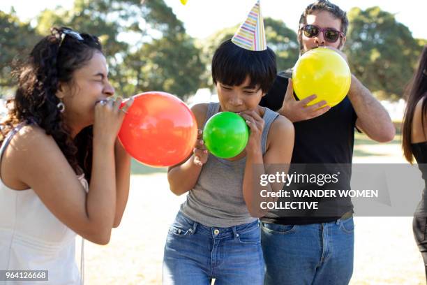 group of multi ethnic friends in the park laughing whilst blowing up balloons. - university student picnic stock pictures, royalty-free photos & images